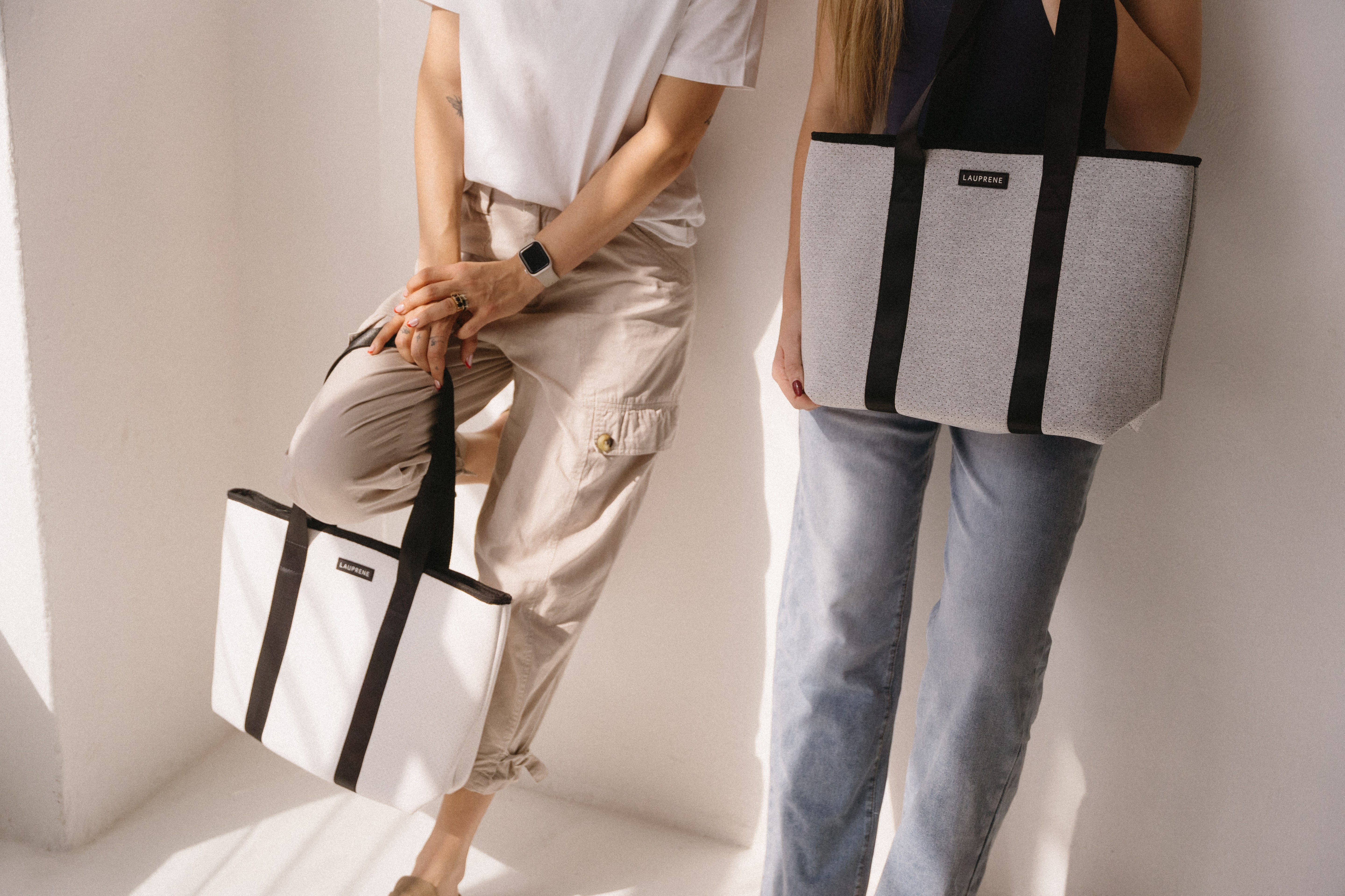 Two people holding tote bags against a white background