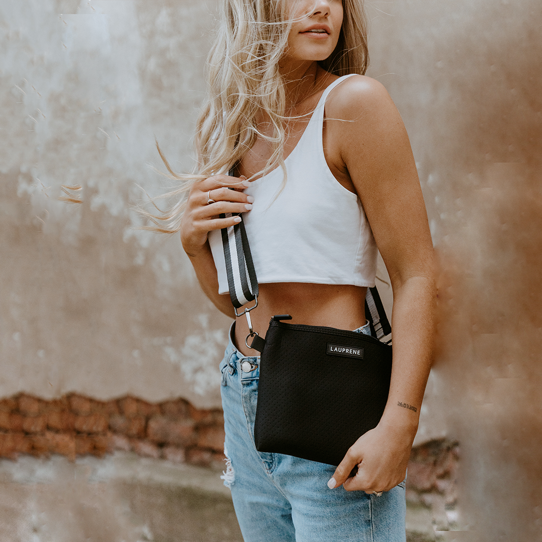 Woman standing with a black crossbody messenger against a old wall