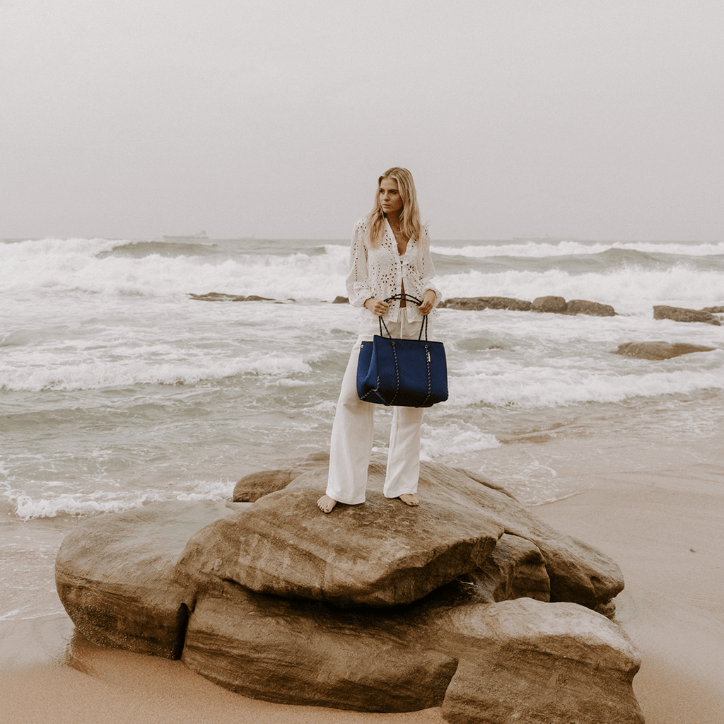 A woman standing on a rock with a blue bag. The bag is a Lauprene Navy classic bag.