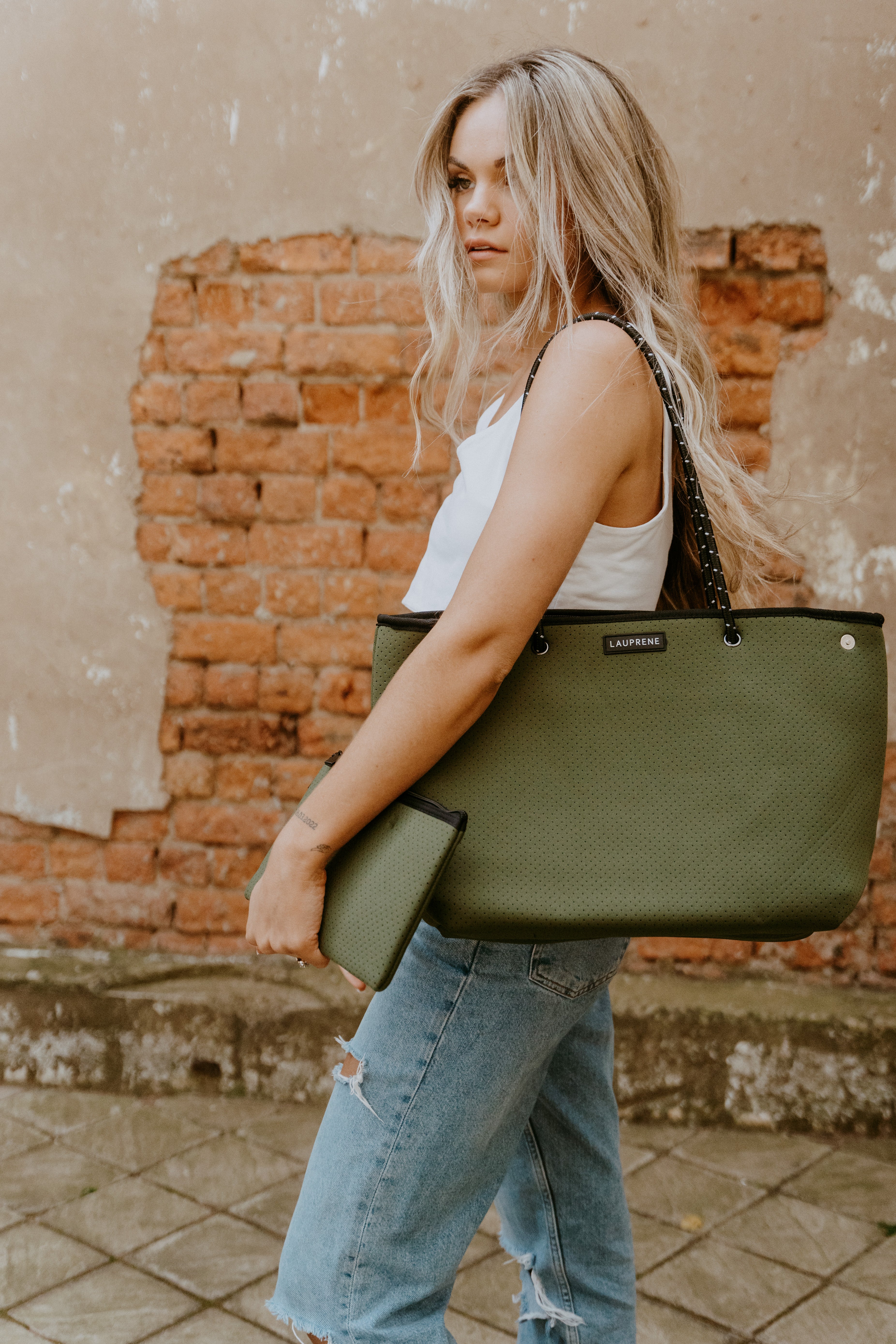 Woman holding a green handbag against a brick wall.