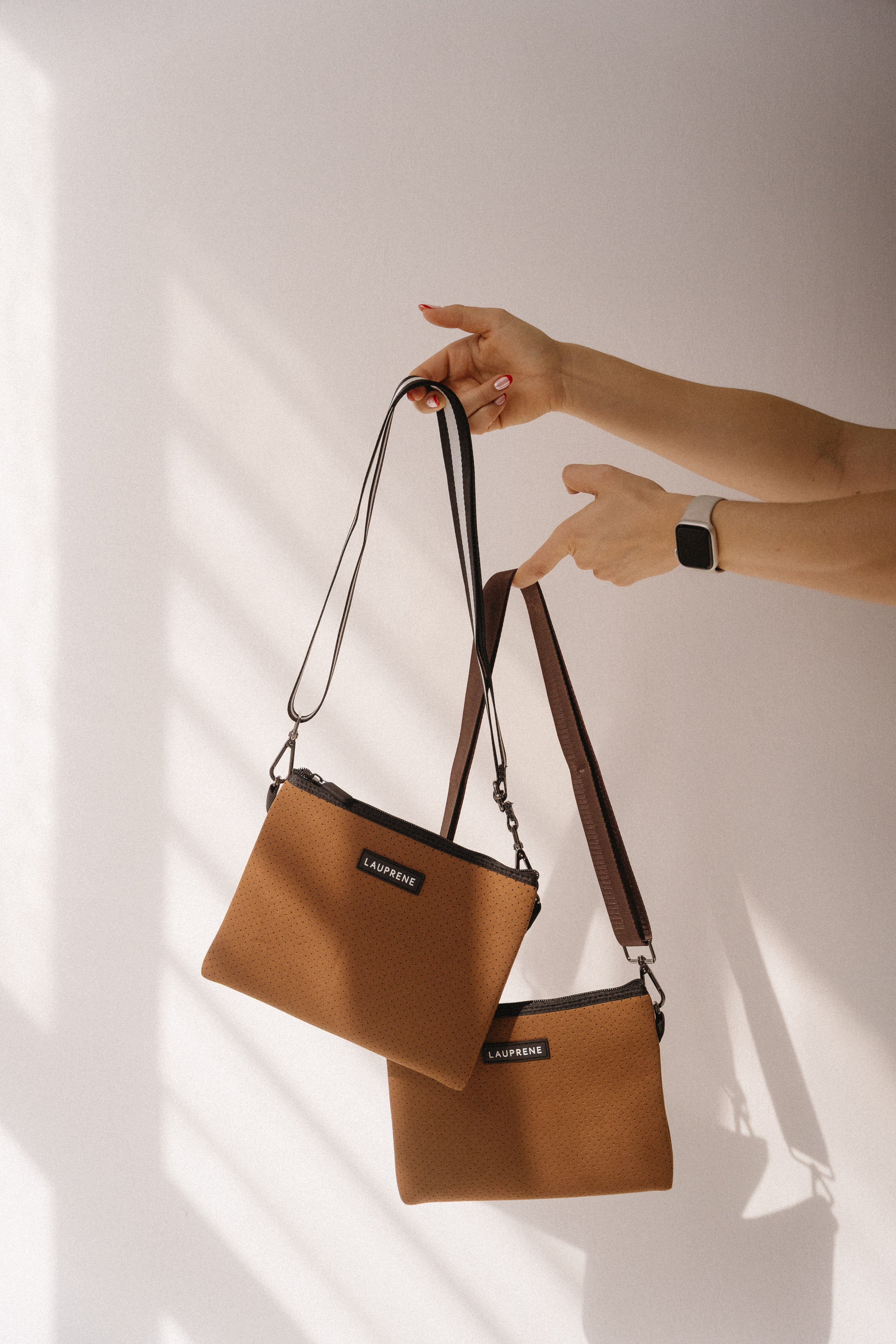 Two brown handbags being held against a white background